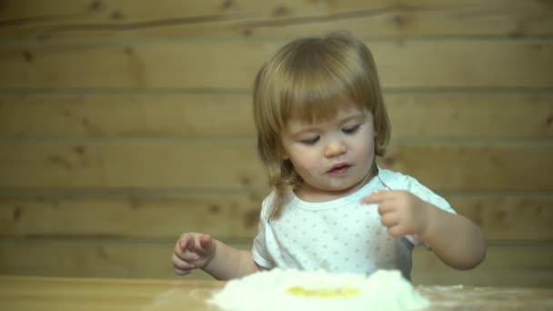 Χαριτωμένο μωρό στην κουζίνα στο τραπέζι σε ένα ξύλινο σπίτι δοκιμάζοντας το αλεύρι — Αρχείο Βίντεο
