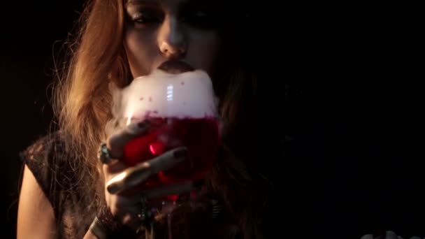 Мистическая женщина, выдувающая жидкий дым над бокалом красного вина — стоковое видео