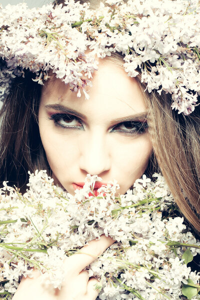Gorgeous female brunette young woman face with spring flowers on sexy lips and lilac wreath on head