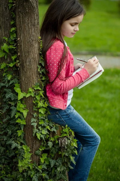 Девушка с блокнотом и ручкой рядом с деревом — стоковое фото