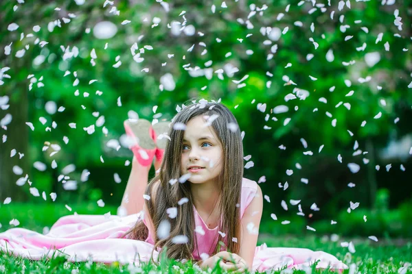 Petite fille sur herbe verte avec des pétales — Photo