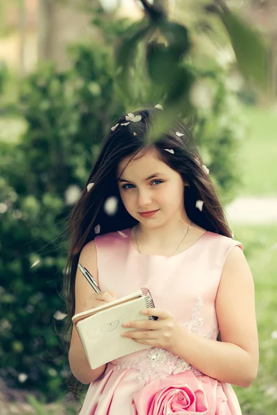 Menina de vestido com caderno e caneta no jardim — Fotografia de Stock