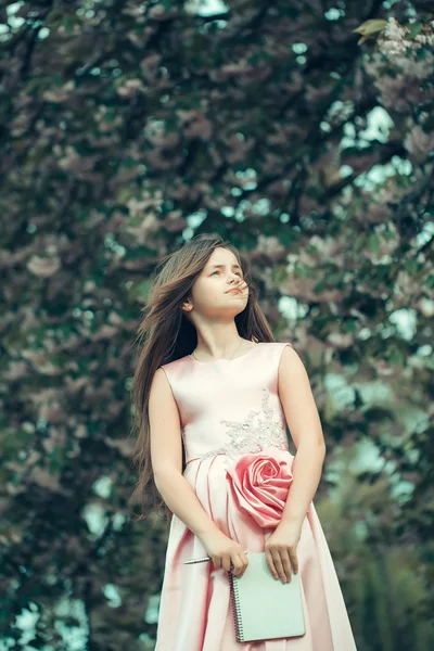 Menina de vestido com caderno e caneta no jardim — Fotografia de Stock