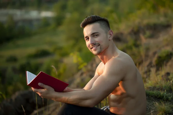 Uomo muscoloso sorridente con libro all'aperto — Foto Stock