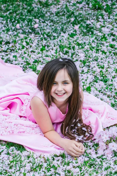 Little girl on green grass with petals — Stock Photo, Image