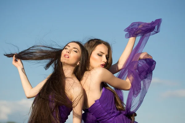 Vrouwen in violet jurken op blauwe hemel — Stockfoto