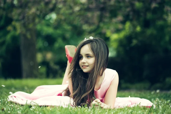 Liten flicka på grönt gräs med kronblad — Stockfoto