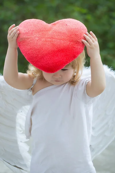 Piccolo ragazzo in ali d'angelo e cuscino del cuore — Foto Stock