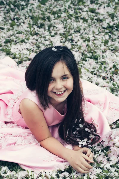 Little girl on green grass with petals — Stock Photo, Image