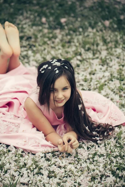 Dziewczynka na zielonej trawie z płatkami — Zdjęcie stockowe