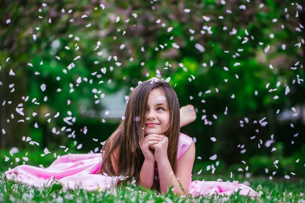 Liten flicka på grönt gräs med kronblad — Stockfoto