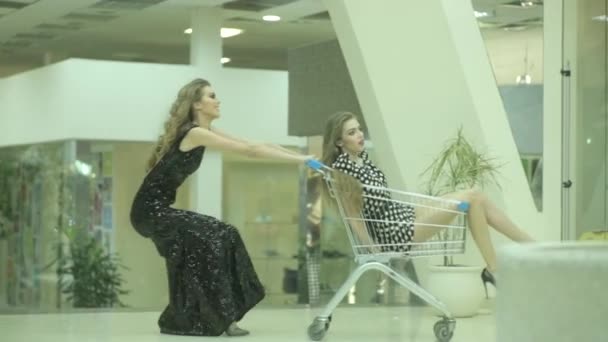 Dos chicas traviesas adictas a la compra con push-cart en vestido de noche elegante — Vídeo de stock