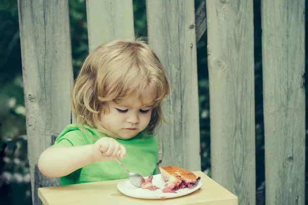 Malý chlapec jíst koláč u dřevěného plotu — Stock fotografie