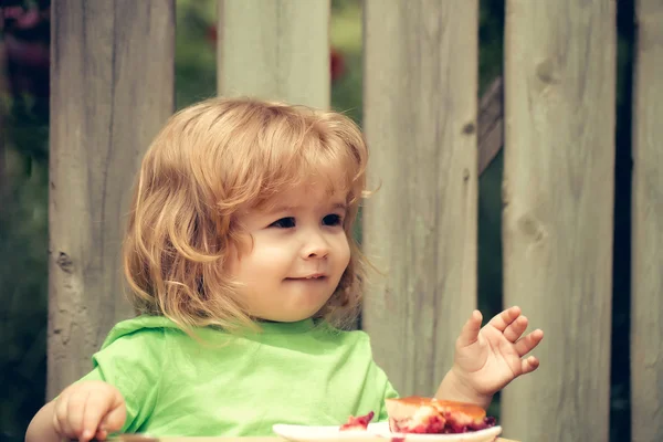 Kleine jongen eten taart in de buurt van houten hek — Stockfoto