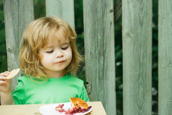 Kleine jongen eten taart in de buurt van houten hek — Stockfoto