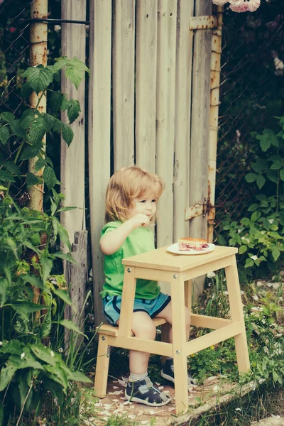 Mały chłopiec jedzenia w pobliżu różany krzew — Zdjęcie stockowe