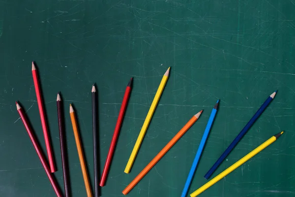 Colorful pencils on green blackboard or desk — Stock Photo, Image
