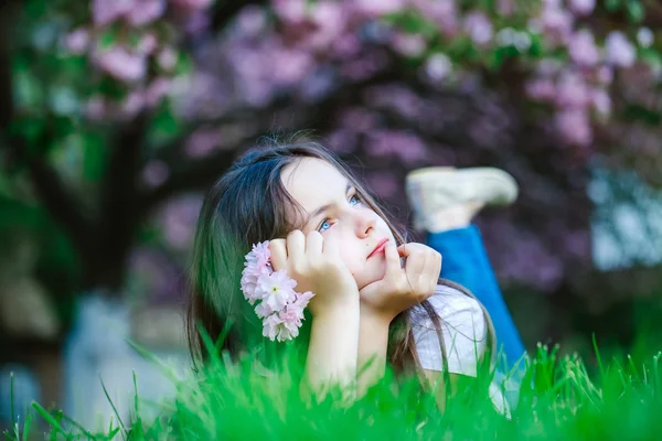 Liten flicka på gräs i blom — Stockfoto