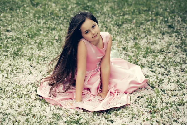 Little girl on green grass with petals — Stock Photo, Image