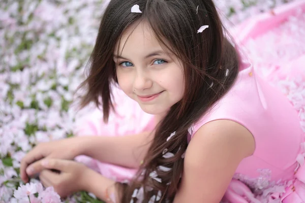 Little girl on green grass with petals — Stock Photo, Image