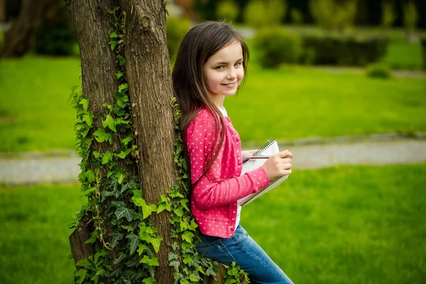 Mädchen mit Notizbuch und Stift in der Nähe von Baum — Stockfoto