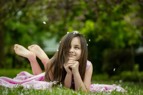 Little girl on green grass with petals — Stock Photo, Image