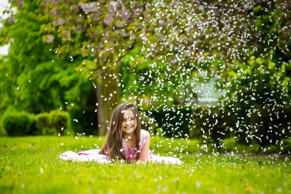 Meisje op groene gras met bloemblaadjes — Stockfoto