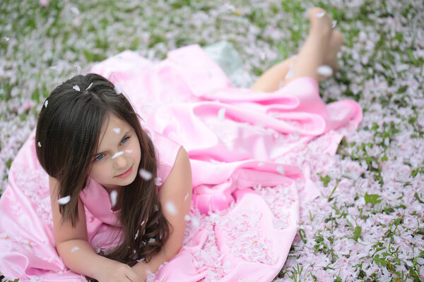 Little girl on green grass with petals