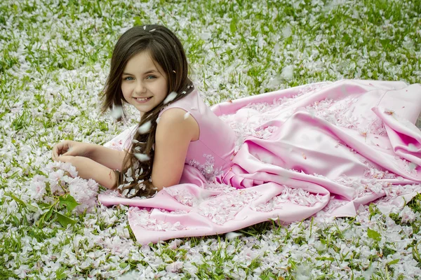 Little girl on green grass with petals — Stock Photo, Image