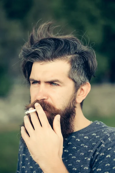 Бородатый мужчина курит сигарету на открытом воздухе — стоковое фото