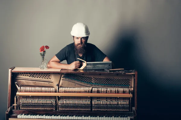 Muž v helmě poblíž piano s pilou a kladivo — Stock fotografie