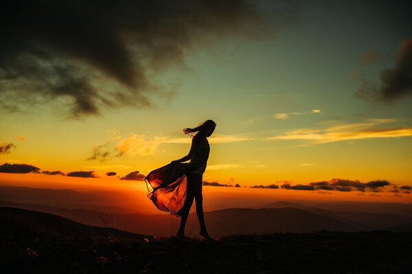Woman or girl silhouette walking at beautiful view on sunset or sunrise in blue sky with clouds and yellow orange sun in mountains on natural background