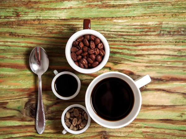 Grão de café em copos e colher na mesa — Fotografia de Stock