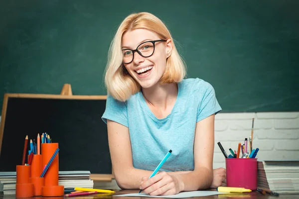 教師は熟練した指導者です。緑の黒板の背景の上にメガネの若い先生。教室で美しい先生。教室で勉強している学生。世界の教師の日. — ストック写真