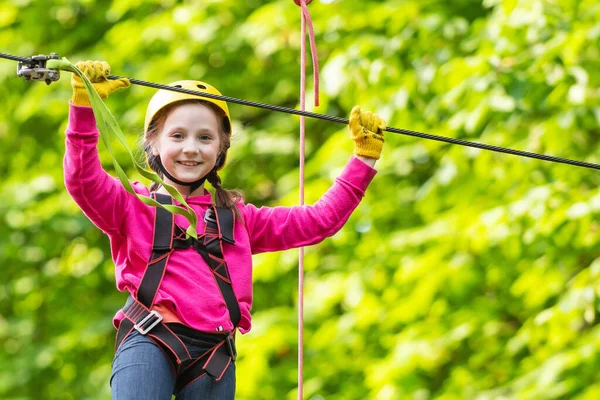 Roping park. Portrait of a beautiful kid on a rope park among trees. Happy Little child climbing a tree. Child. Safe Climbing extreme sport with helmet.