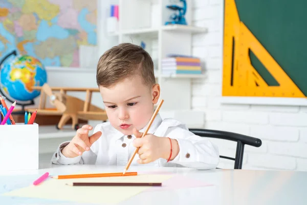 Geconcentreerde schooljongen zit aan het bureau en schrijft. Schooljongen studeert huiswerk tijdens haar les thuis. — Stockfoto