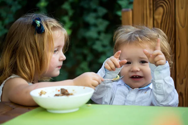 Kind voeden baby met lepel. Twee kleine kinderen, schattig peuter meisje en grappige baby jongen, samen eten, zus voeden van de broer, gezond ontbijt. — Stockfoto