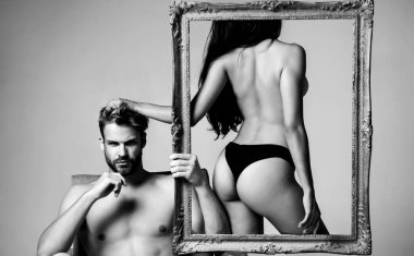 Çerçevede seksi popolu çıplak seksi kız. Yakışıklı, kaslı sakallı adam seksi bir kadınla çerçeveyi tutuyor. Soyut sanat. Gri arka planda izole edilmiş seksi çift.