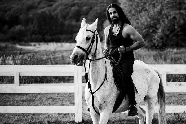 Attractive man sitting on white horse on the ranch in autumn. Full length of young handsome man sitting on his stallion at the country side. Man equestrian on his horse riding at nature. — Stock Photo, Image