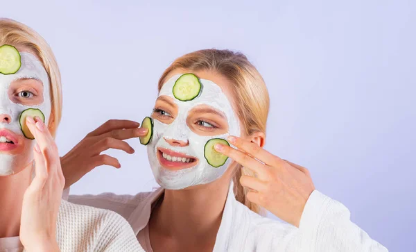 Концепція догляду за шкірою за допомогою свіжих кілець огірків та білої маски на обличчі. Дві сестри мають вихідні в спальні . — стокове фото