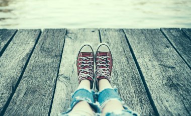 Kırmızı spor ayakkabılı bir çocuk bir çocuk kampında dinleniyor. Şehir dışındaki göl manzaralı spor ayakkabılı bir genç. İyi kamp ve seyahatler. Hafta sonu konsepti.