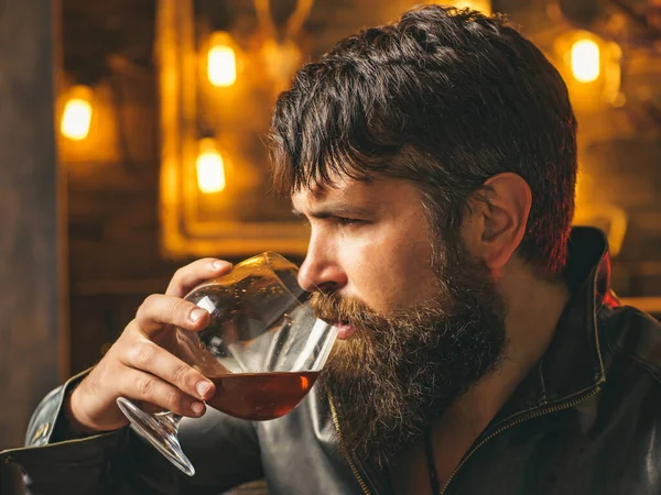 Man drinks brandy or whiskey. Bearded man wearing jacket and drinking whiskey brandy or cognac. Serious man having alcohol and nicotine addiction. Stop alcohol and smoking addiction.