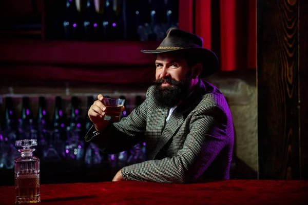 Mann mit Bart hält Glasschnaps in der Hand. Bartträger trinken Cognac. Mann mit einem Glas Whisky. Whisky schlürfen. Porträt eines Mannes mit dickem Bart. Machotrinken. Degustation, Verkostung. — Stockfoto