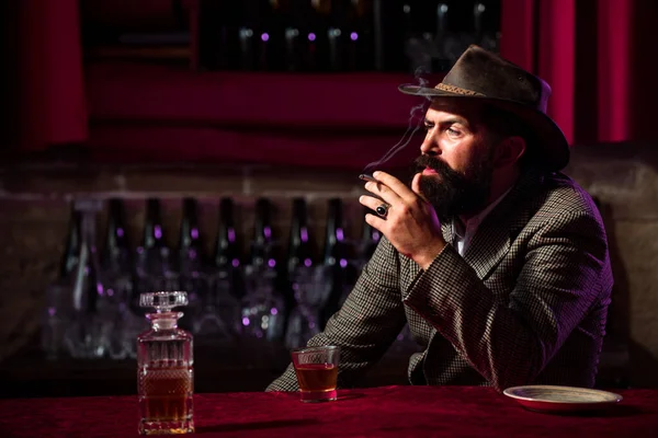 Handsome bearded man enjoying whiskey in bar. Hipster with beard drinking a brandy in bar. Brutal guy drinking alcohol. — Stock Photo, Image