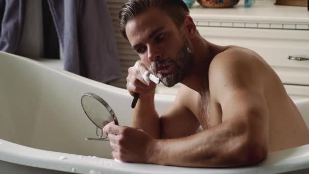 Beau jeune homme barbu rasage barbe en peignoir dans la salle de bain. — Video