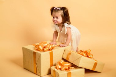 Büyük hediye kutusuyla şık giyinmiş, güzel gülümseyen bir bebek. Sarı arka planda izole edilmiş, kopyalama alanı. Doğum günü hediyesi.