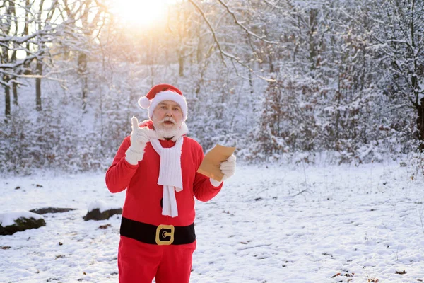Santa Claus leyendo wis hlist y llegando al bosque de invierno con una bolsa de regalos, paisaje de nieve. —  Fotos de Stock