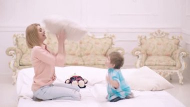Anne ve oğlu yatakta zıplayıp yastık fırlatıyorlar. Mutlu bir aile. Anneler Günü. Çocuk yardımı ve çocukların bakımı. Anne ve oğulun ilişkisi. Annen seni seviyor..