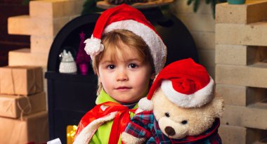 Oyuncak ayısıyla küçük mutlu çocuk kameraya bakıyor. Çocuklar için kış teslimatı. Noel hediyesi kutulu mutlu çocuk. Noel 'i kutlayan şirin çocuklar. Noel Kutlaması