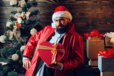 Sakallı modern Noel Baba mutlu noeller ve mutlu yıllar diler. Noel kutlaması, tatil. Noel ağacı arkaplanı. Kırmızı Noel Baba hediye kutusuyla.